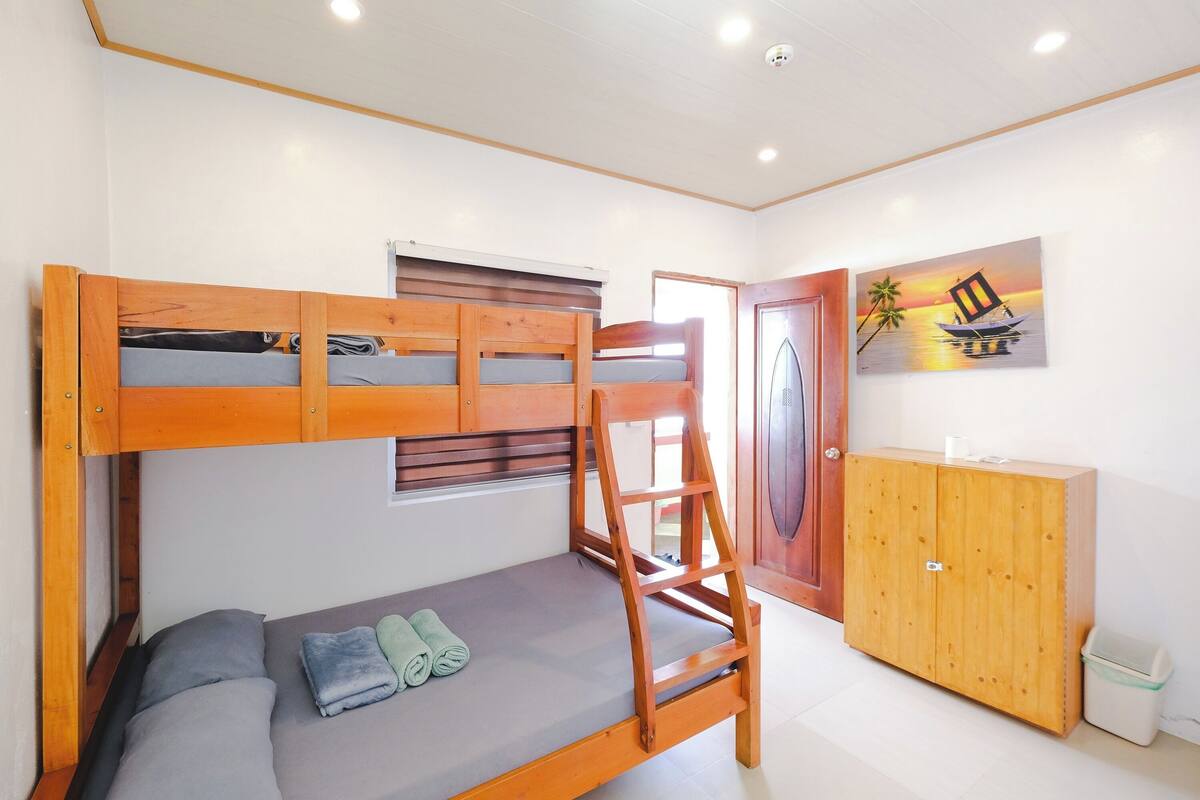 Una cama litera con estructura de madera, un colchón gris y dos toallas enrolladas.