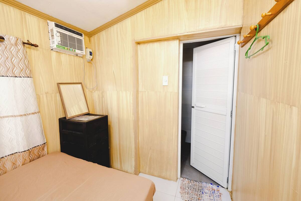Un dormitorio con cama, mesita de noche, equipo de aire acondicionado, armario y puerta que da a otra habitación.