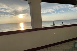 A balcony with a view of the sea at sunset, a white pillar, and a small sailboat. - Monaliza Surf Resort By Zuzu (San Juan)