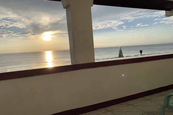 Un balcón con vistas al mar al atardecer, un pilar blanco y un pequeño velero.