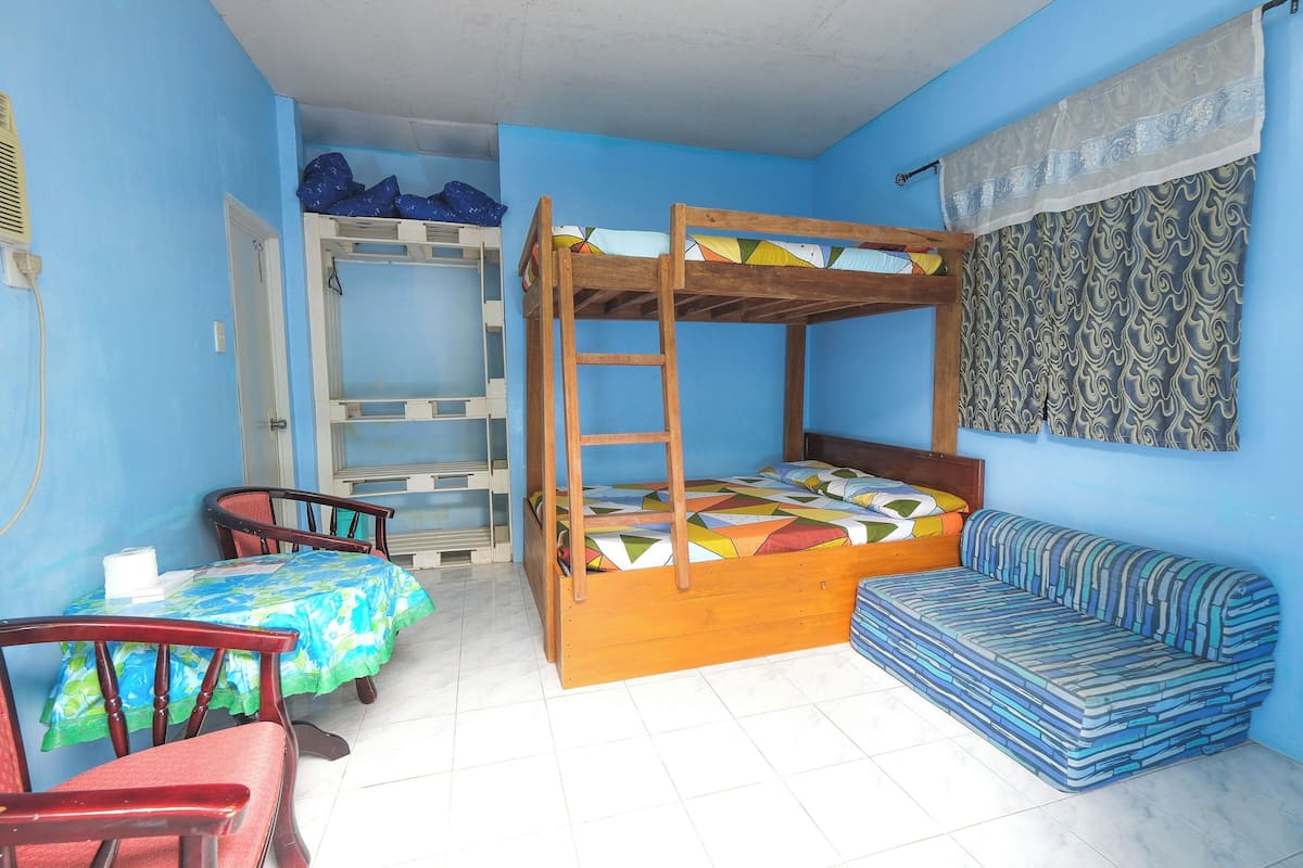 Una habitación con literas, un sofá, una mesa con sillas y una cortina estampada.