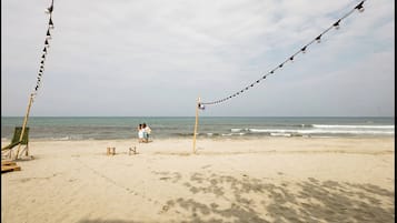 A beach with a row of lights, a wooden chair, and a couple sitting on the sand.