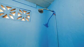 Un mur bleu avec une pomme de douche et une fenêtre ornée d’un motif géométrique.