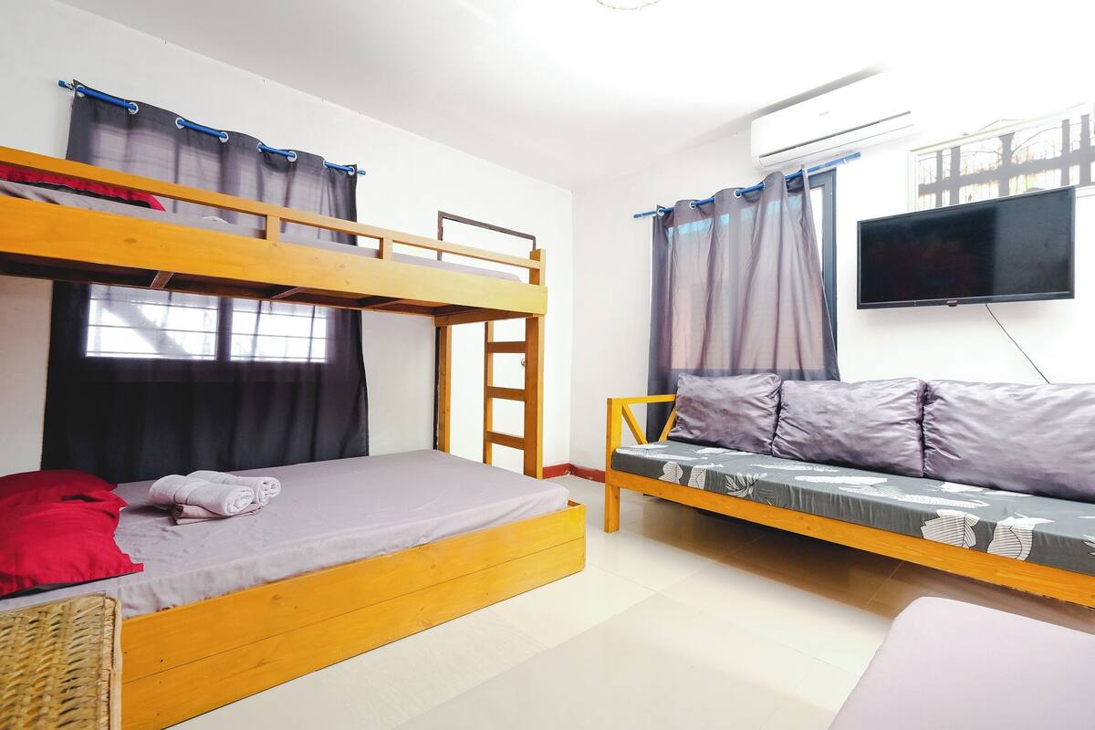 Una habitación con literas, un sofá, un televisor y una ventana con cortinas.