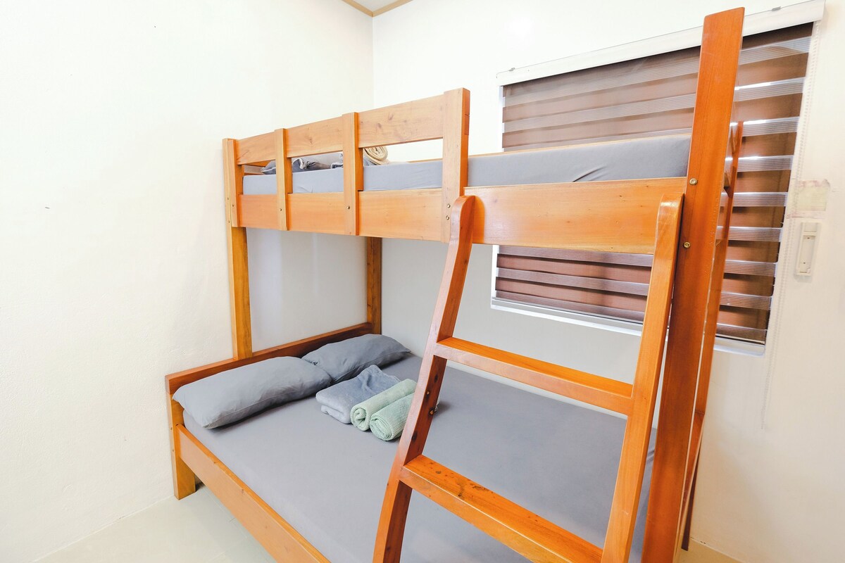 A bunk bed with a wooden frame, a window with blinds, and a small table attached to the bed.