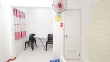 A small, clean room with a white door, a table with two chairs, a fan, and a shower curtain.