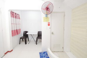 A small, clean room with a white door, a table with two chairs, a fan, and a shower curtain. - Monaliza Surf Resort By Zuzu (San Juan)