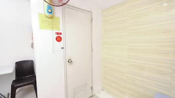 A room with a white door, a black chair, a fan, and a tiled floor.