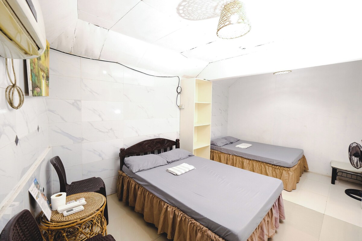 A hotel room with two beds, a chair, a small table, and a ceiling fan.