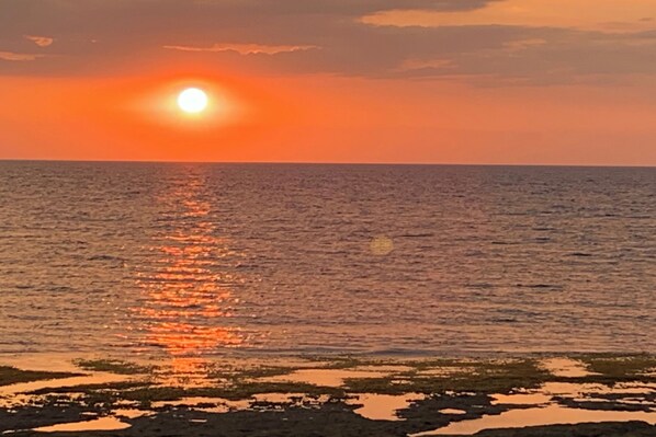 A sunset over a calm sea with a rocky shoreline. - Monaliza Surf Resort By Zuzu (San Juan)