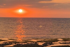 A sunset over a calm sea with a rocky shoreline. - Monaliza Surf Resort By Zuzu (San Juan)