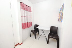 A small room with a white table and two wicker chairs, a red and white curtain, and a colorful painting on the wall. - Monaliza Surf Resort By Zuzu (San Juan)
