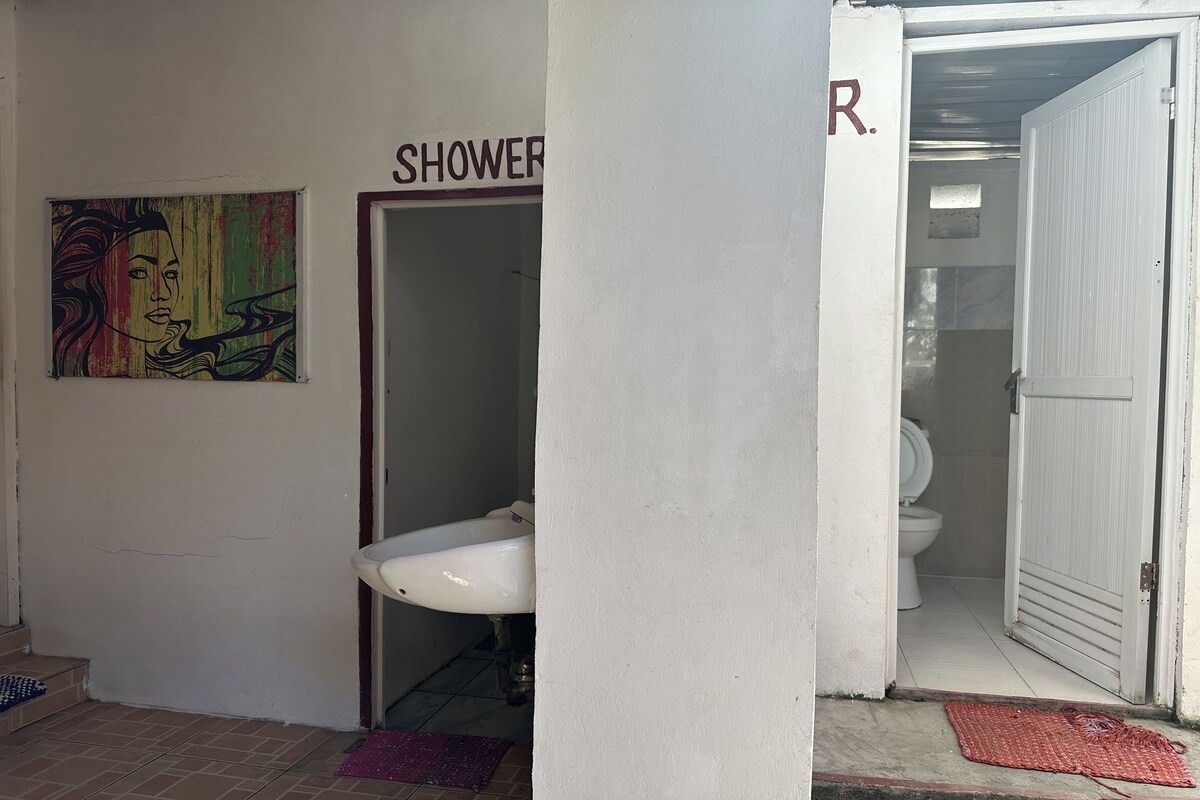 A bathroom with a white sink, a shower area, and a toilet. There is a colorful artwork on the wall above the sink.