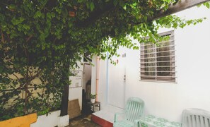 A small, enclosed outdoor area with a white wall, a window with bars, a green plastic chair, and a small table. - Monaliza Surf Resort By Zuzu (San Juan)