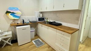 Una cocina compacta con armarios blancos, microondas, refrigerador pequeño y encimera de madera.