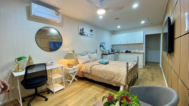 Un dormitorio pequeño con cama, mesita de noche, lámpara, silla y un escritorio con computadora.