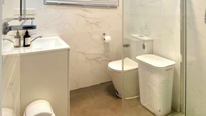 Un baño moderno con cabina de ducha de vidrio, inodoro y lavamanos con espejo.