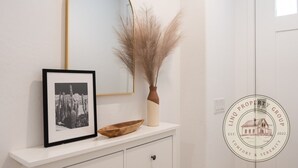 Ein gerahmtes Foto, eine Vase mit getrocknetem Pampasgras und eine Holztasse auf einem weißen Konsolentisch.