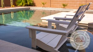 Ein Poolbereich mit weißen Adirondack-Stühlen und dem Logo von 'Liqnq Property Group' auf dem Boden.