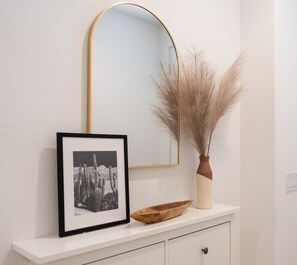 A framed photograph, a vase with dried pampas grass, and a wooden bowl on a white console table. - Private Retreat House with Pool and Spa/Hot Tub Min from Westgate, Andretti Karting, and TWoods Golf (Phoenix)