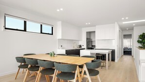 A modern kitchen with white cabinets, a wooden dining table with six chairs, and a view of the living area.