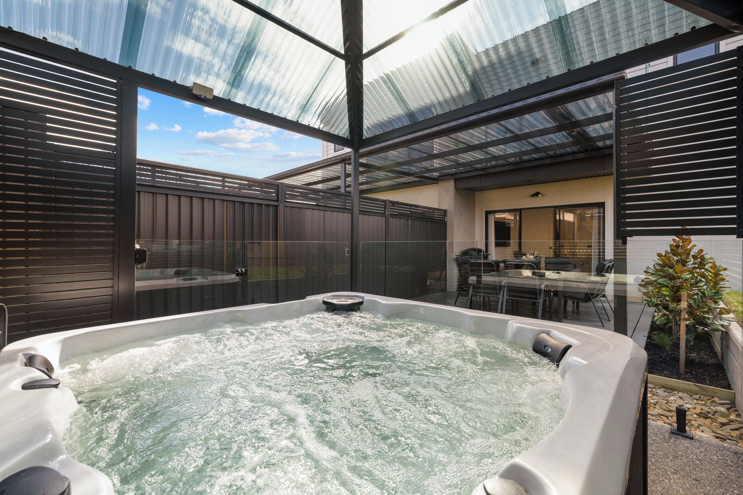 A hot tub area with a glass ceiling, a wooden fence, and a patio with outdoor furniture.