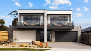A modern two-story house with a garage, large windows, and outdoor seating.