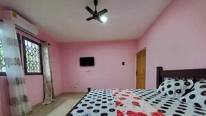 Quarto com cama, ventilador de teto, janela com cortinas e televisão fixada na parede.