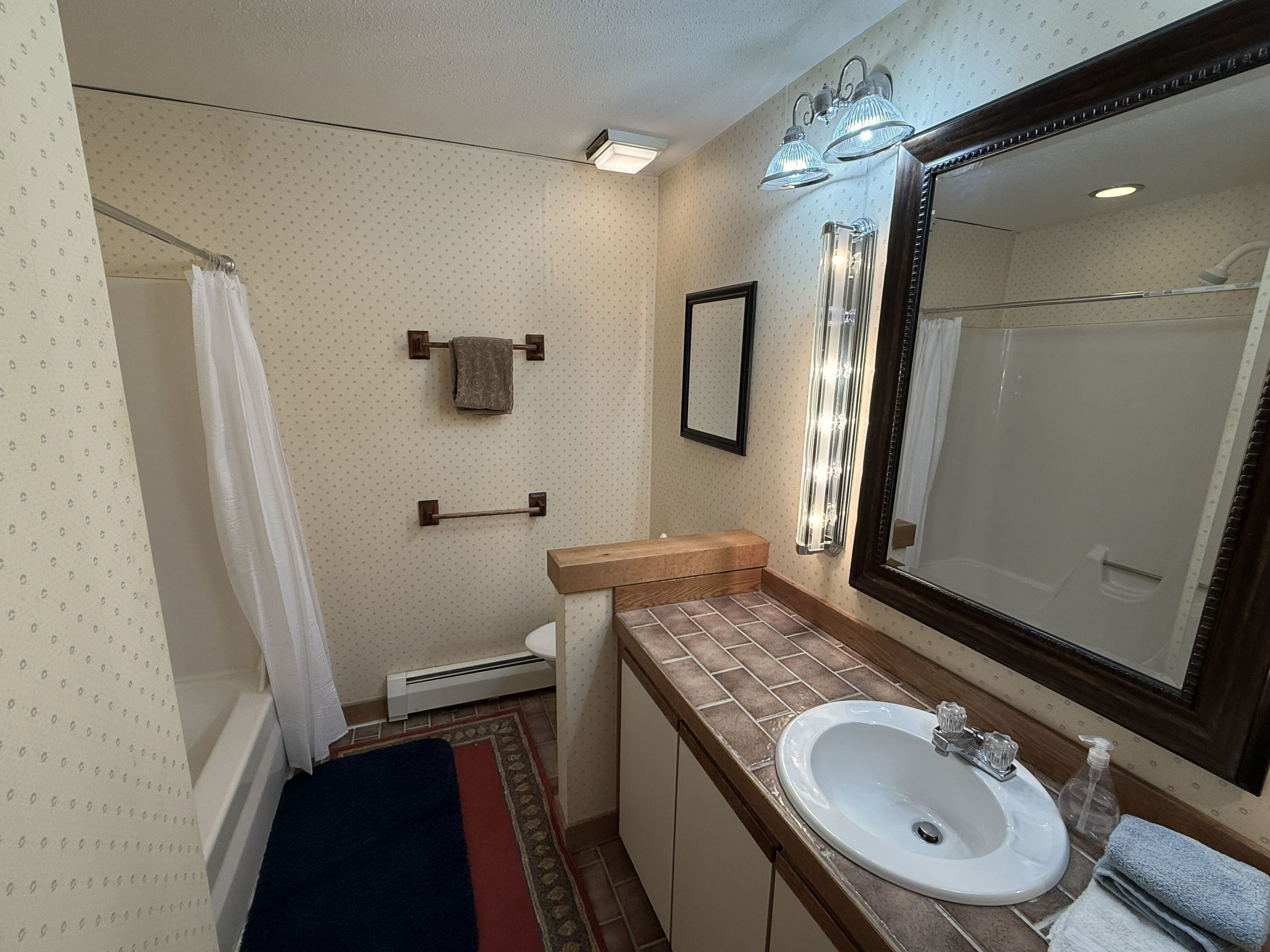 Un baño con un espejo grande, un lavamanos y una ducha.