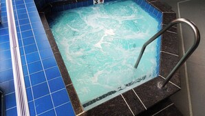 Un jacuzzi con un borde de azulejos azules y una escalera metálica.