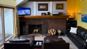 Una sala de estar con chimenea, sofás de cuero, televisor y pared de acento amarilla.