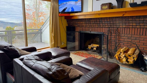 Una sala de estar acogedora con sofás de cuero, chimenea, televisor y vistas al exterior.