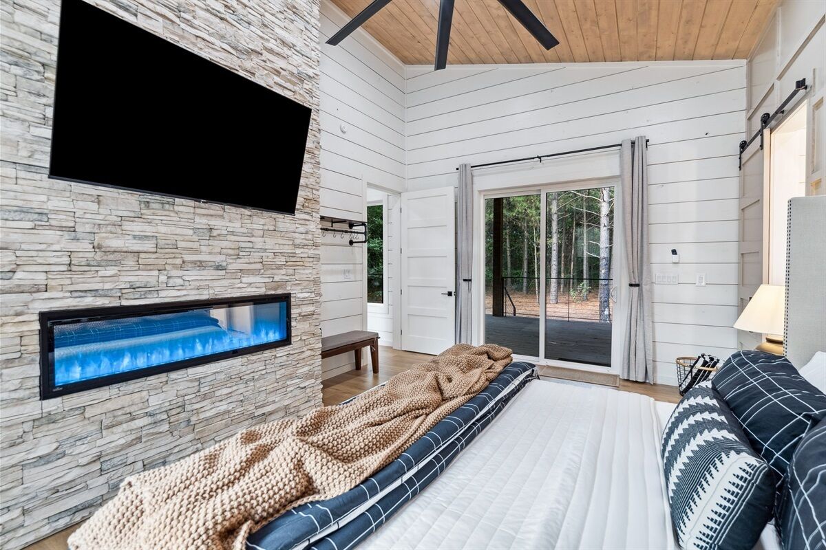 Une chambre avec un mur en pierre, un téléviseur à écran plat, un grand lit recouvert d’une couverture à motifs et une vue sur l’extérieur.
