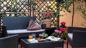 A wicker outdoor seating area with a sofa, chairs, and a table set with drinks, snacks, and a magazine. - CHARME HOLIDAYS PUCCINI (Rome)