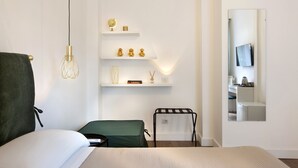 A hotel room with a bed, a green chair, a small table, a shelf with decorative items, and a mirror reflecting a TV and a desk. - CHARME HOLIDAYS PUCCINI (Rome)