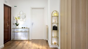A hallway with a wooden door, a glass and metal console table with decorative items, and a wooden wardrobe. - CHARME HOLIDAYS PUCCINI (Rome)