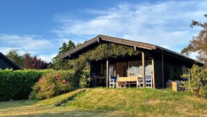 Une maison moderne dotée d’un porche abrité, entourée d’une végétation luxuriante et surplombée d’un ciel bleu azur.