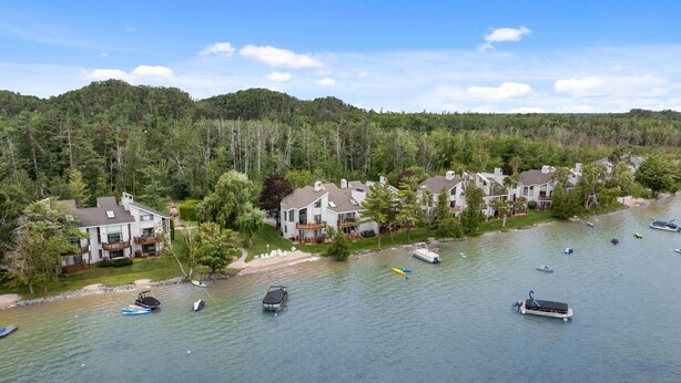 Un barrio residencial junto al lago, con casas a lo largo de la orilla, barcos en el agua y una colina boscosa al fondo.