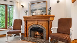 Una habitación acogedora con chimenea, dos sillones a rayas, un cuadro y una ventana con vistas a árboles.