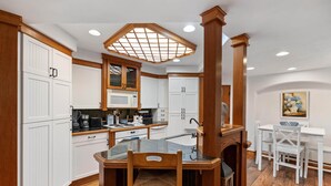 Una cocina con armarios blancos, microondas, lavabo y comedor con mesa y sillas.