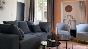 Un salon moderne avec un canapé gris, deux fauteuils, une table basse et une grande fenêtre avec des rideaux.