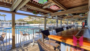 Zona de bar con vista a la piscina, terraza de madera y asientos al aire libre.