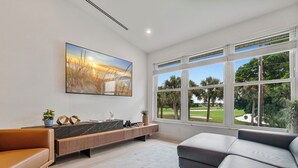 A modern living room with a large window, a painting, a sofa, and a console table. - NEW! Golf View Getaway Condo, 3 bedrooms, 2 bathrooms, heated pool (Naples)