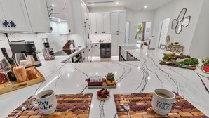 A modern kitchen with white cabinets, a marble countertop, and a central island with a fruit bowl and a coffee mug. - NEW! Golf View Getaway Condo, 3 bedrooms, 2 bathrooms, heated pool (Naples)