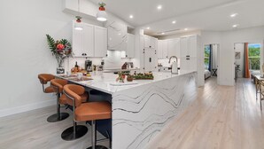 A modern kitchen with white cabinets, a marble island, and bar stools. - NEW! Golf View Getaway Condo, 3 bedrooms, 2 bathrooms, heated pool (Naples)