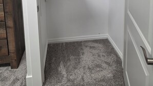 Un placard d’angle avec trois étagères, une porte en bois et un sol recouvert de moquette.