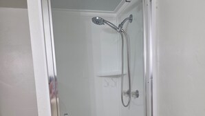 Une douche fermée par des parois en verre, équipée d’un pommeau de douche à main et d’un pommeau de douche fixe.