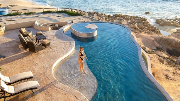 A pool with a curved design, surrounded by lounge chairs and a seating area.