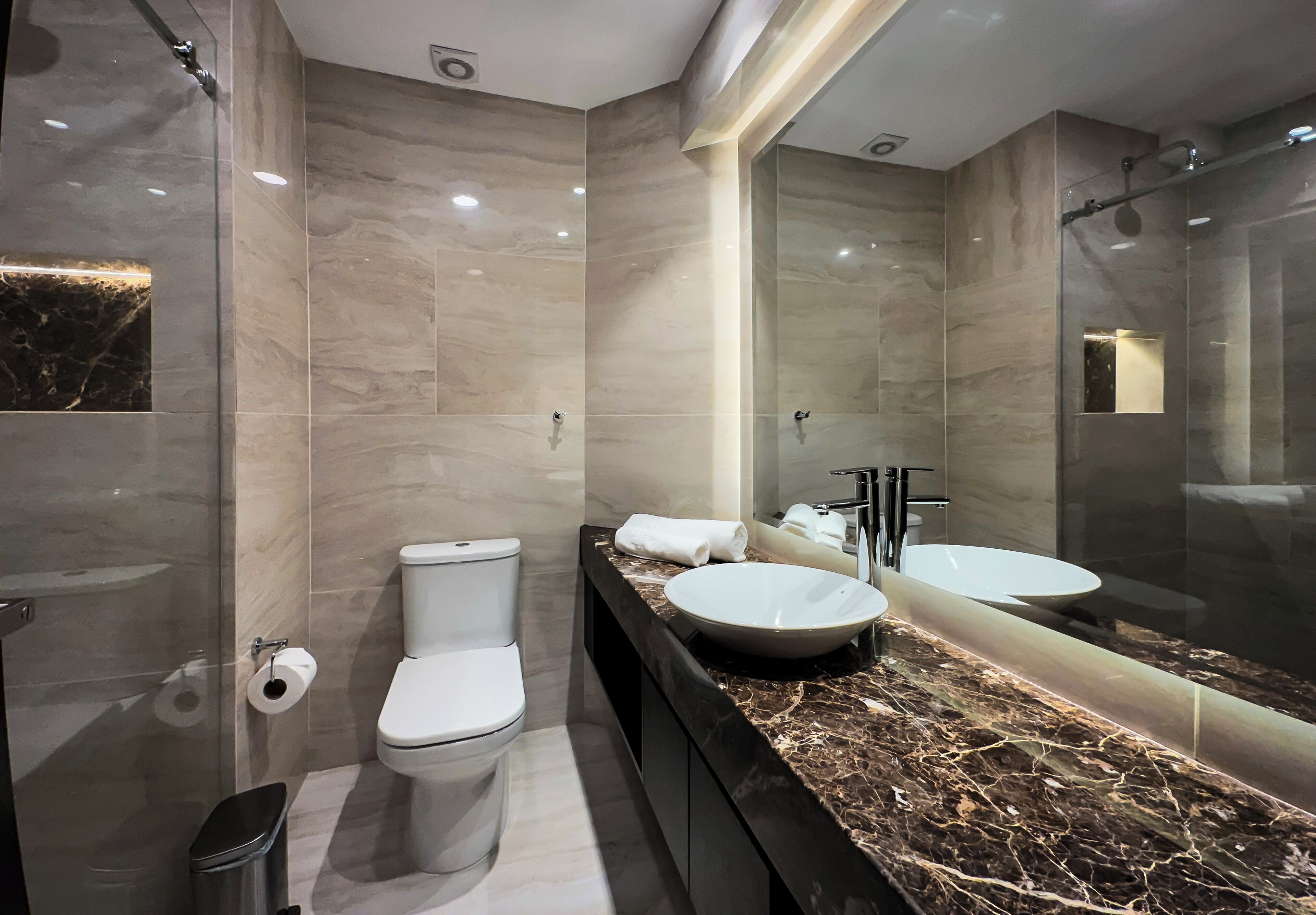 A modern bathroom with a marble vanity, a large mirror, a toilet, and a shower area.