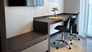 A modern office space with a dark wood desk, a black office chair, a flat-screen TV mounted on the wall, and an air conditioning unit. - AMERICA APARTMENTS (Santa Cruz)